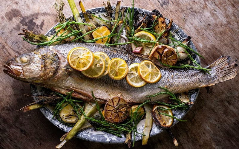 Whole baked sea bass with fresh herbs and lemon, finished with ARLO culinary argan oil for a Mediterranean-inspired main dish